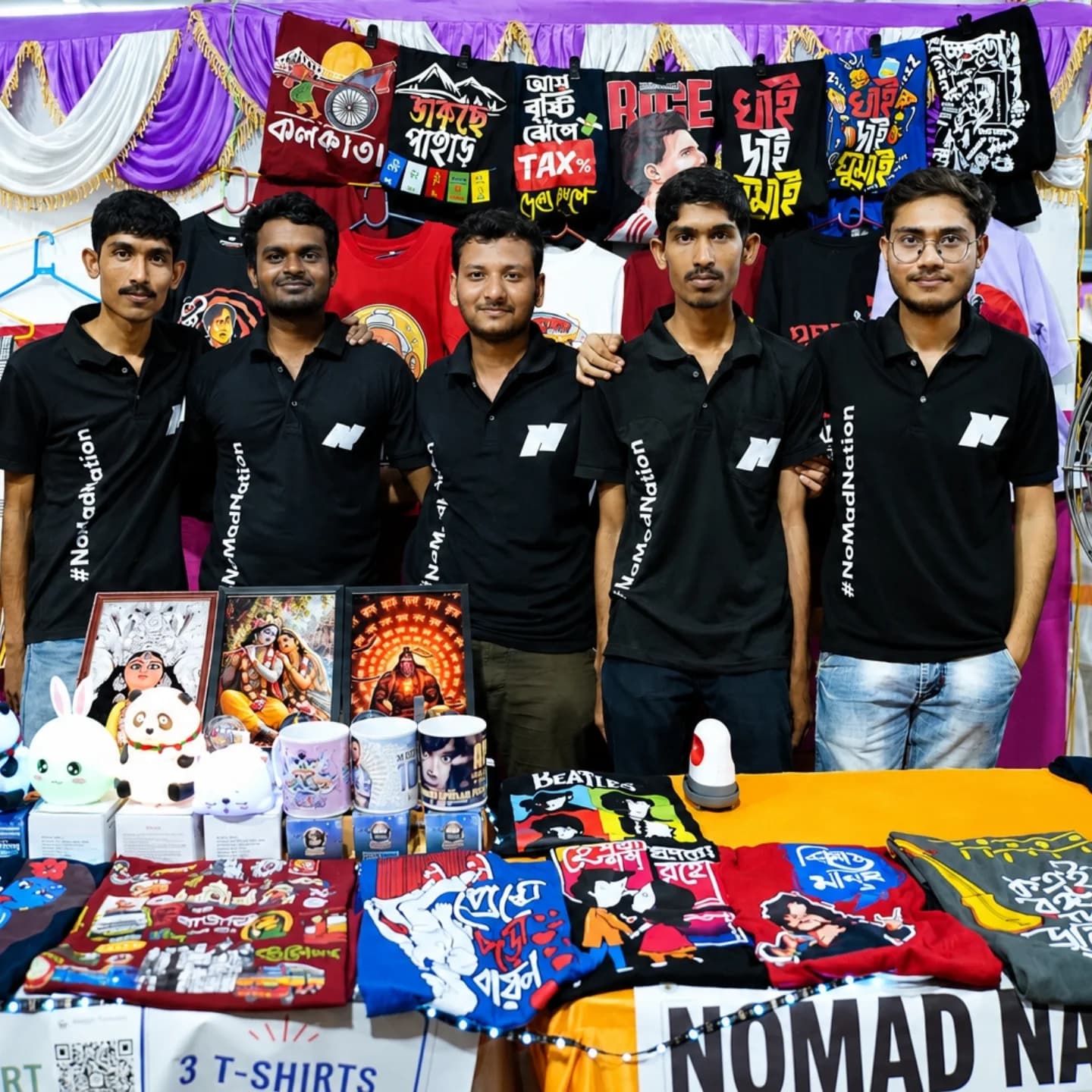 Five members of the Nomad Nation team in branded polos at their stall, surrounded by printed T-shirts, mugs and framed art
